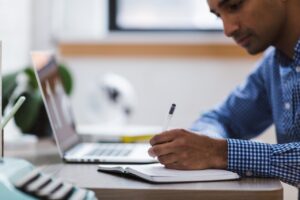 A man writes in a notebook in front of a laptop while learning about data-driven DEI