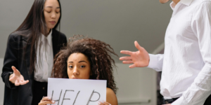 Worker Holds Up Sign For Help As Toxic Colleagues Surround Her