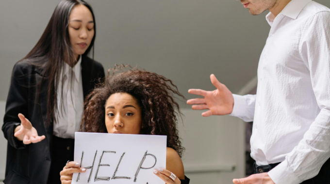 Worker Holds Up Sign For Help As Toxic Colleagues Surround Her